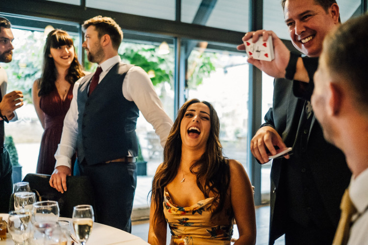 A beautiful girl is laughing at a magic trick at a wedding in the Cotswolds